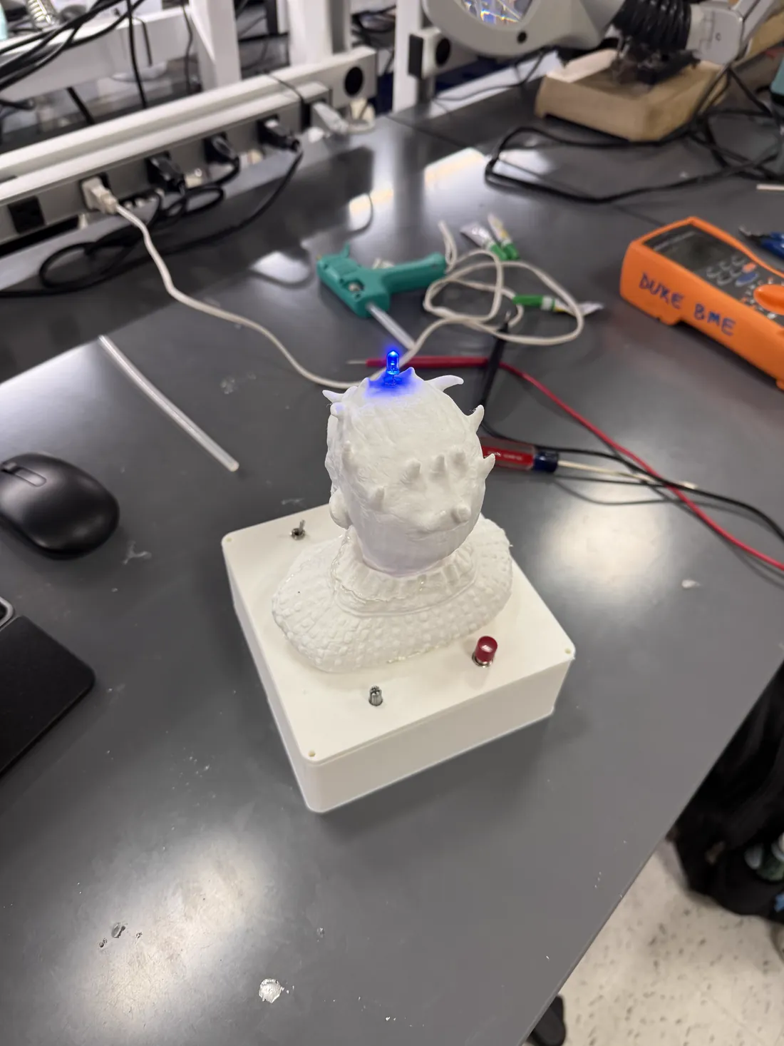 The finished lightbox on a lab bench — a white 3D-printed figure on a printed base, with a blue LED lit at the crown.