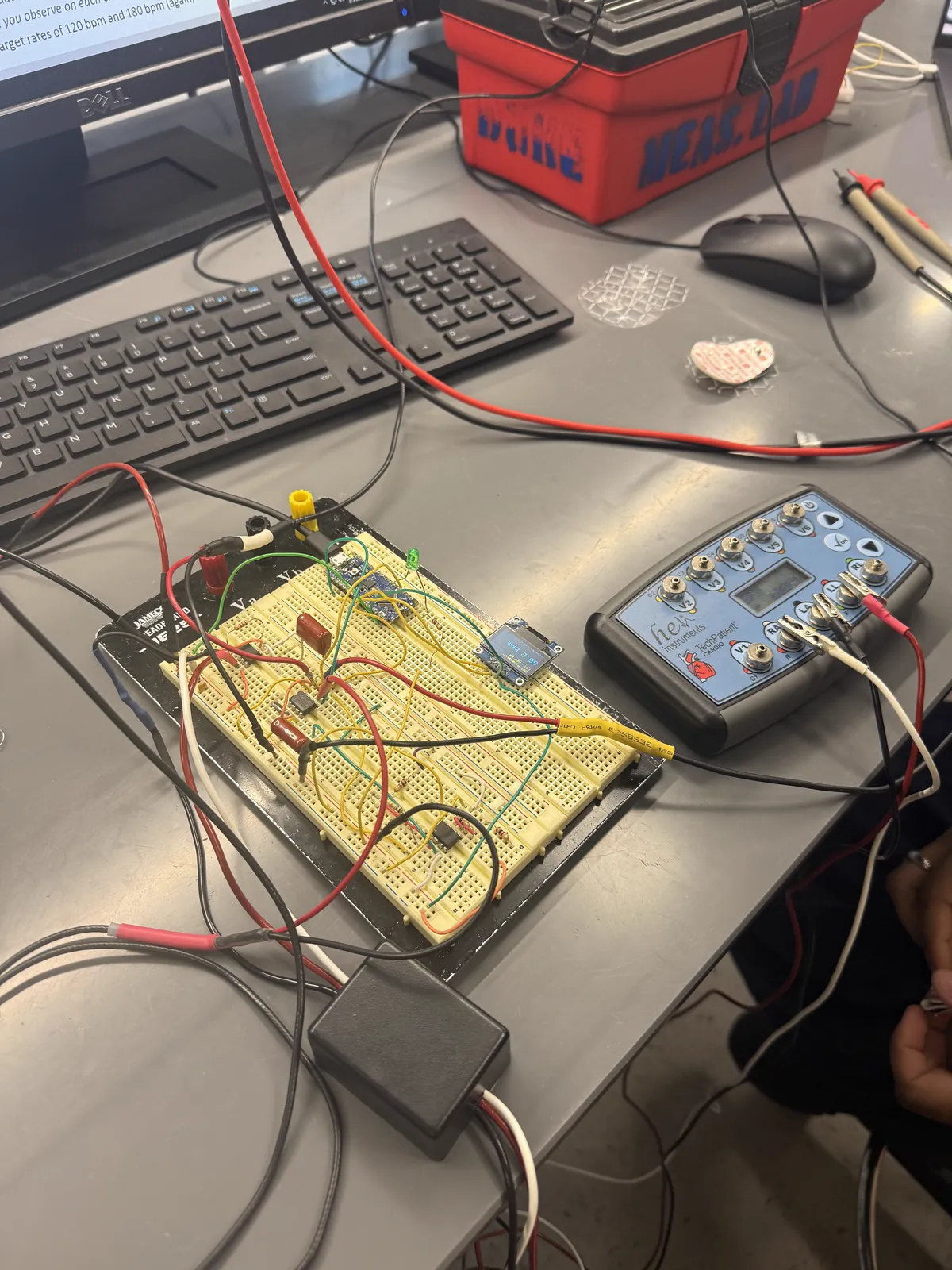 The pacemaker on a lab bench: a breadboard carrying the analog front end and an Arduino Nano Every, a small OLED, and a cardiac patient simulator wired in beside it.