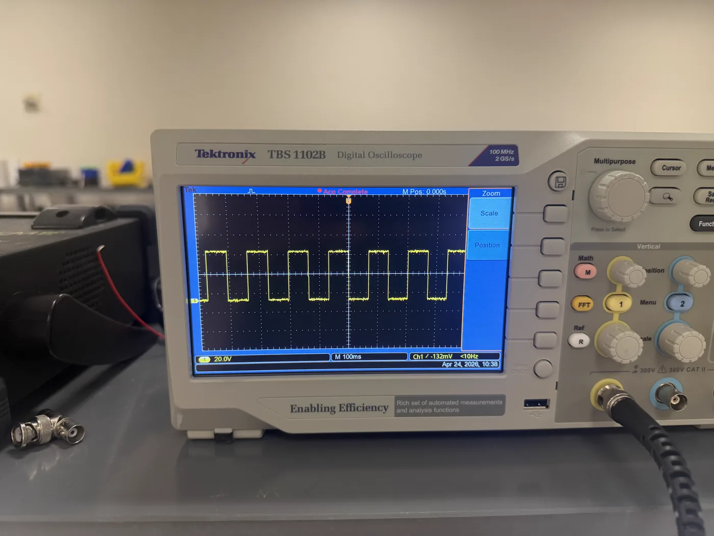 A Tektronix TBS 1102B oscilloscope on a lab bench displaying a clean square wave across the screen at 20 V per division and 100 ms per division.